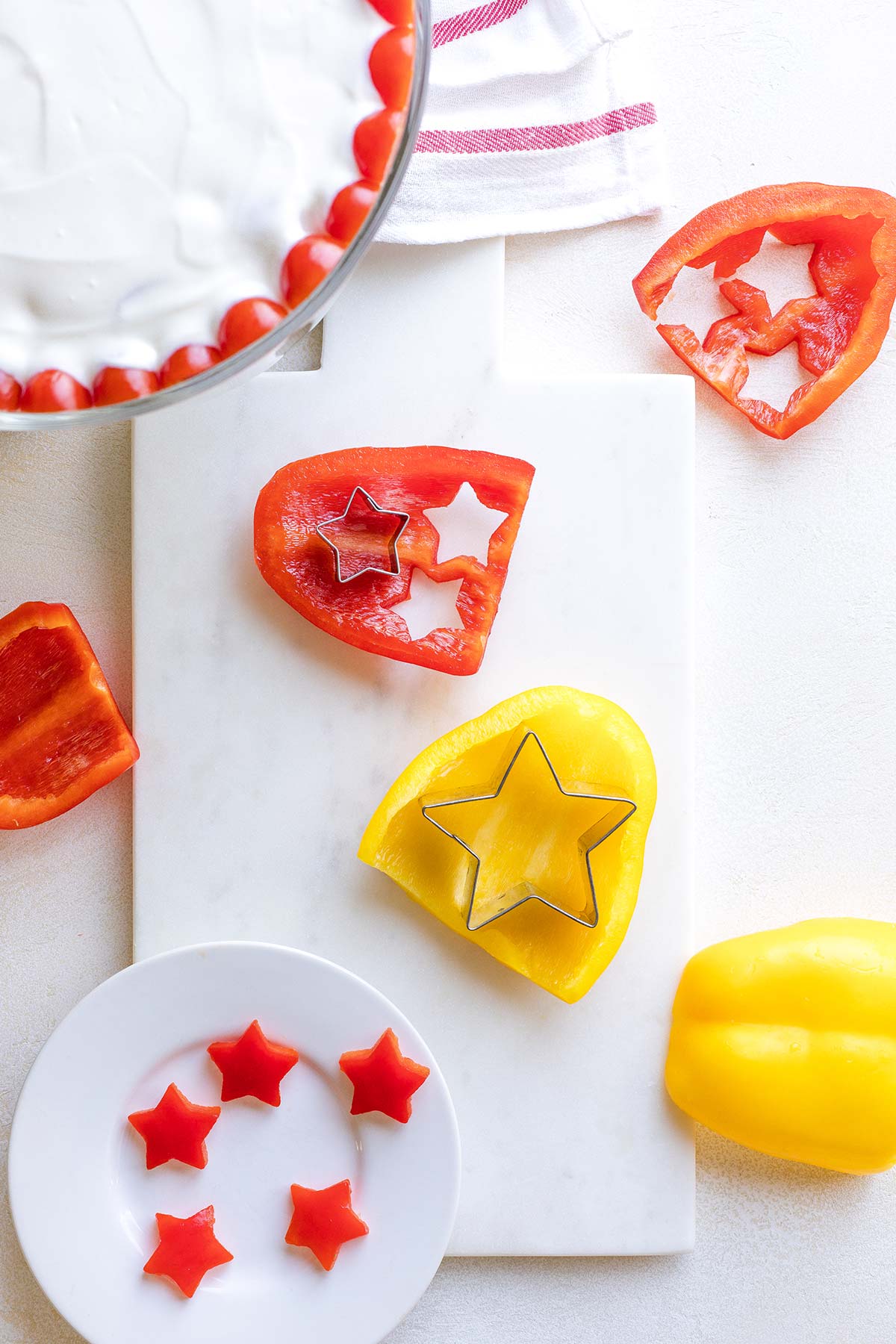 Overhead of cookie cutters cutting star shapes out of flat sides of red and yellow pepper.