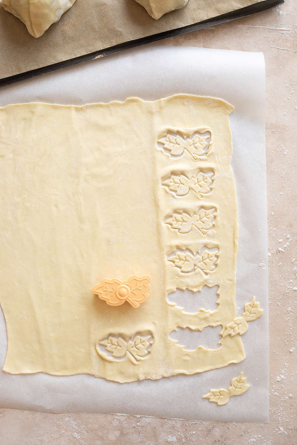 Small orange, leaf-shaped pastry cutter cutting out decorative leaves to put on top of the beef Wellingtons.