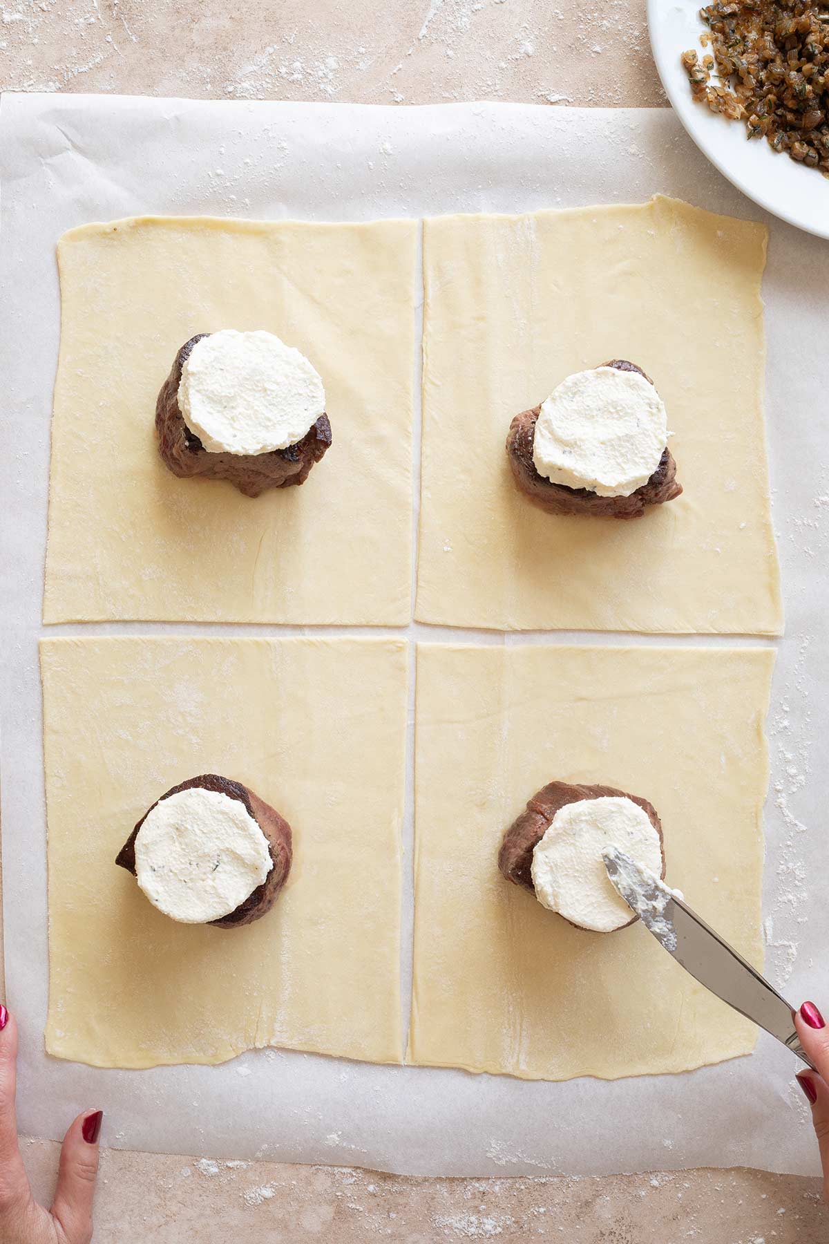 Knife spreading cheese on top of each filet mignon.