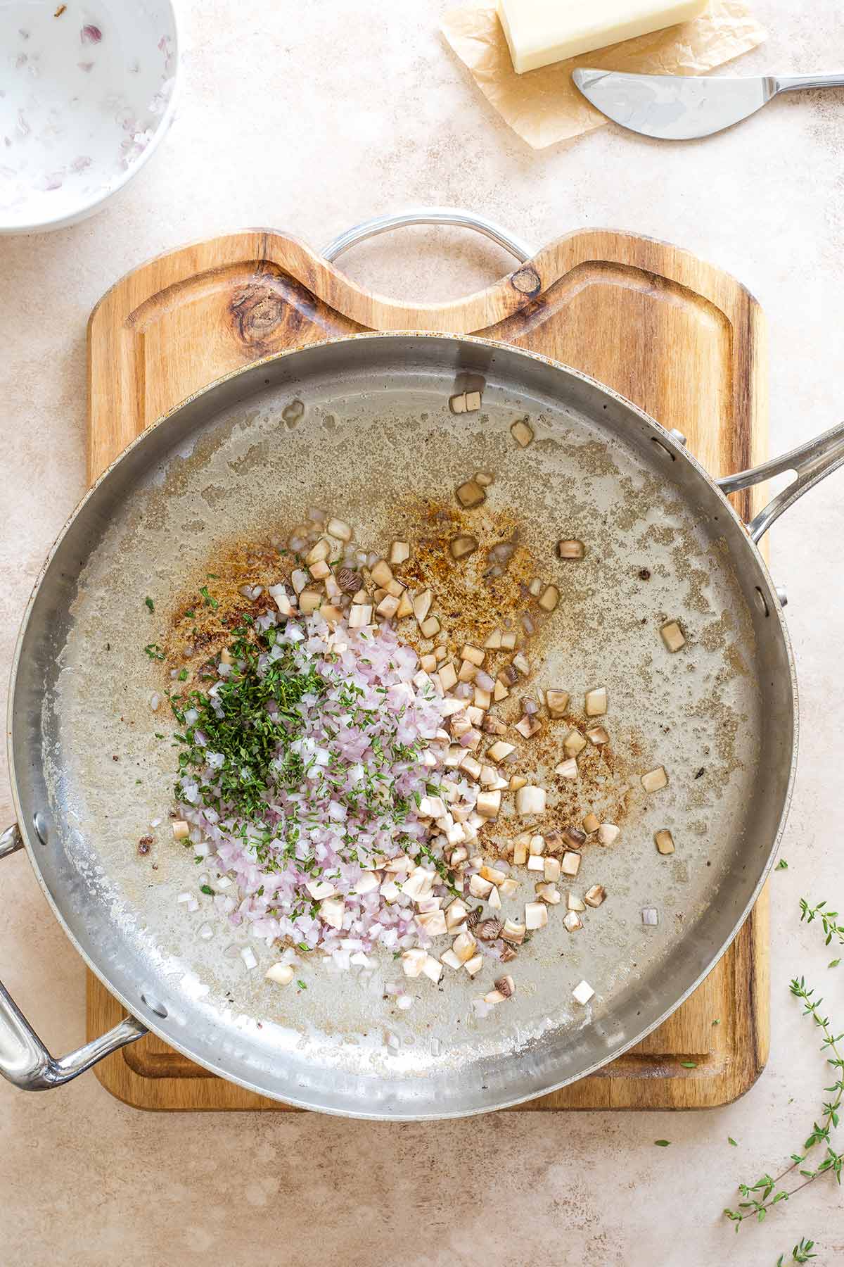 Overhead of duxelles ingredients (butter, shallots, mushrooms, thyme) just added to skillet to cook.