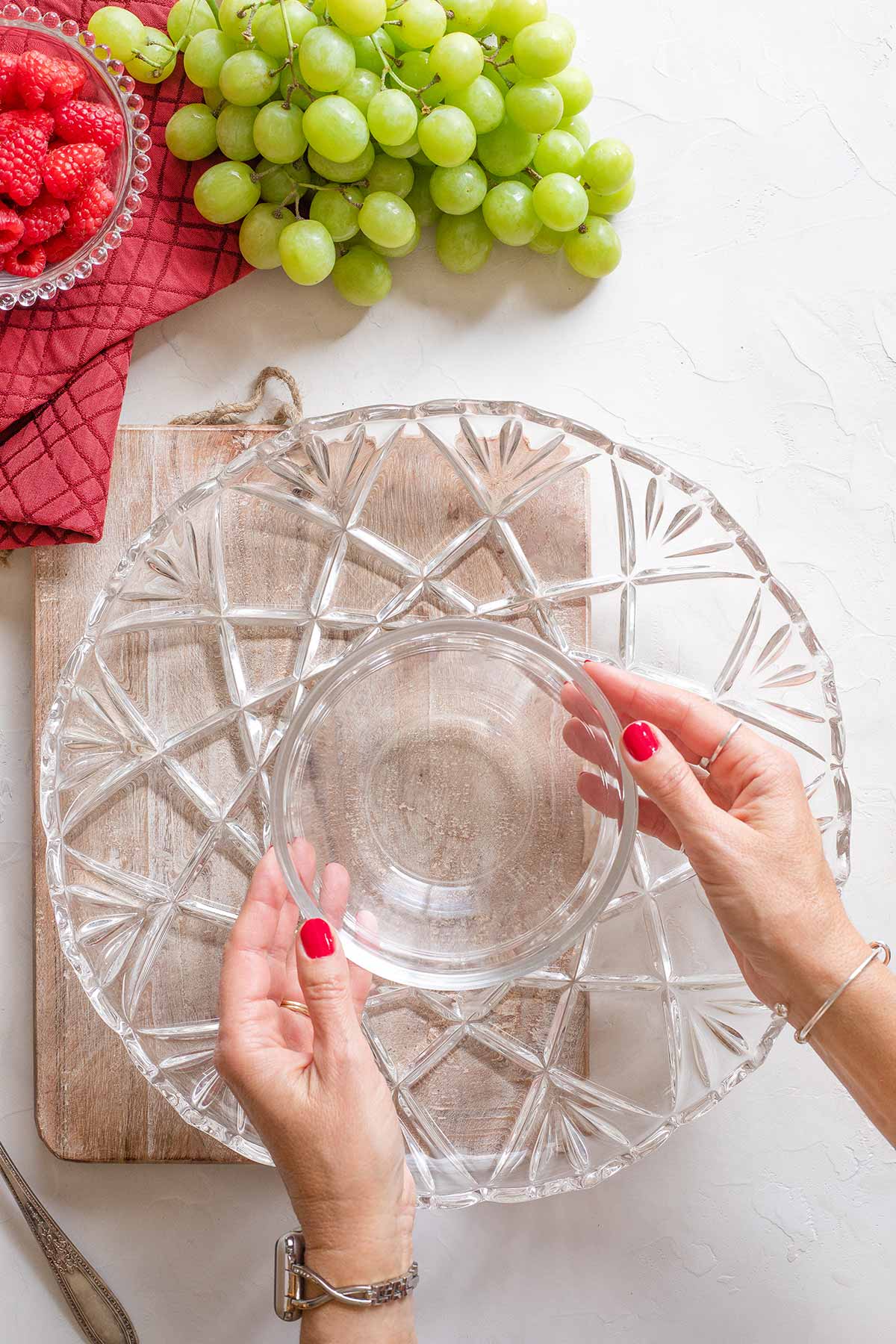 Hands positioning bowl at center of serving platter; grapes and raspberries nearby.