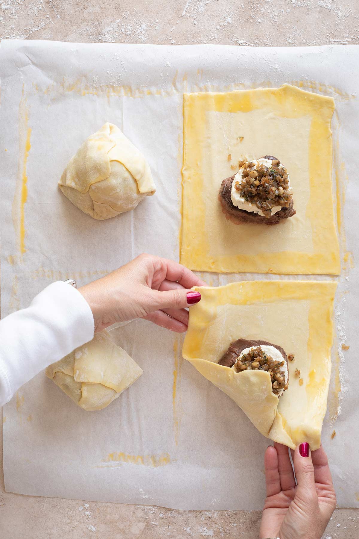 Two hands folding in each puff pastry section to enclose each beef Wellington.