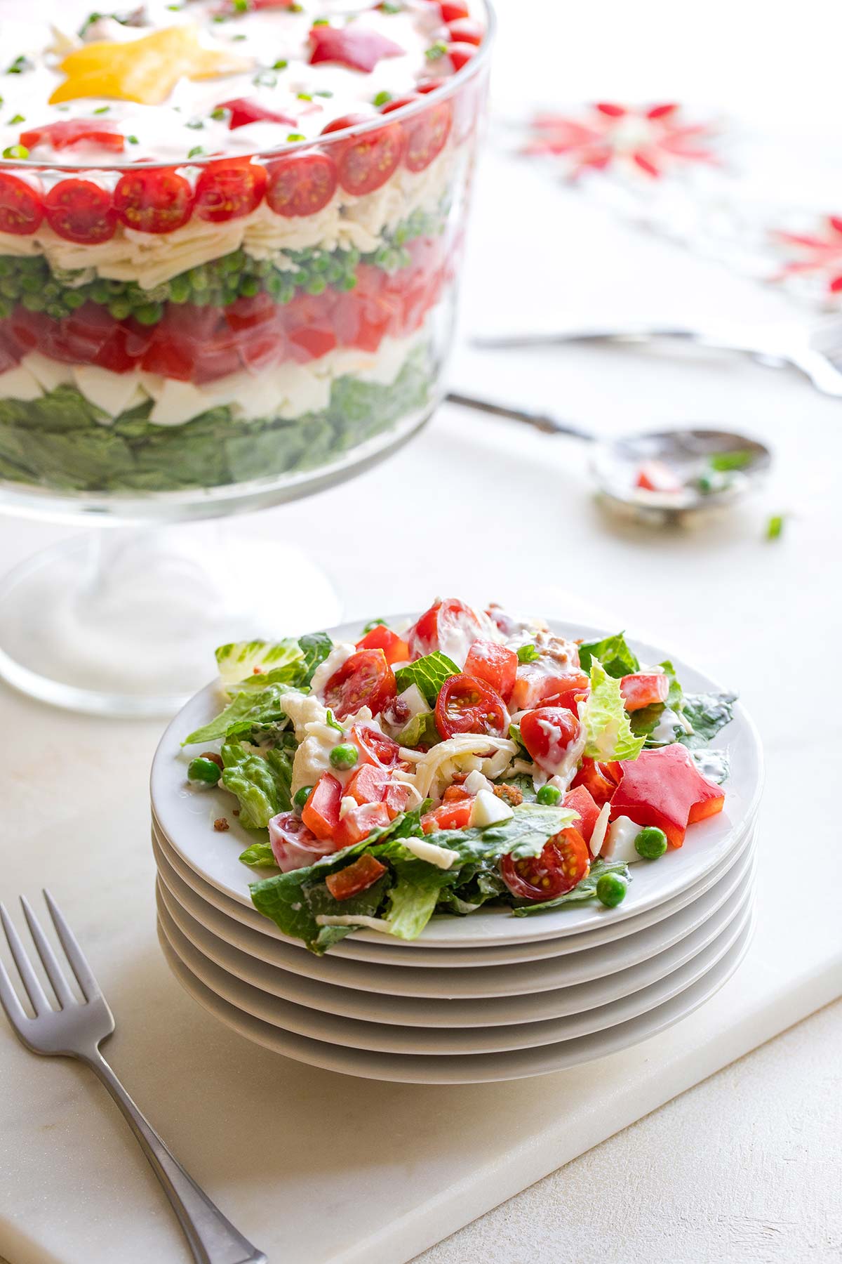 Plated serving of salad on top of stacked plates with serving bowl of salad behind and Christmas tablecloth in background.