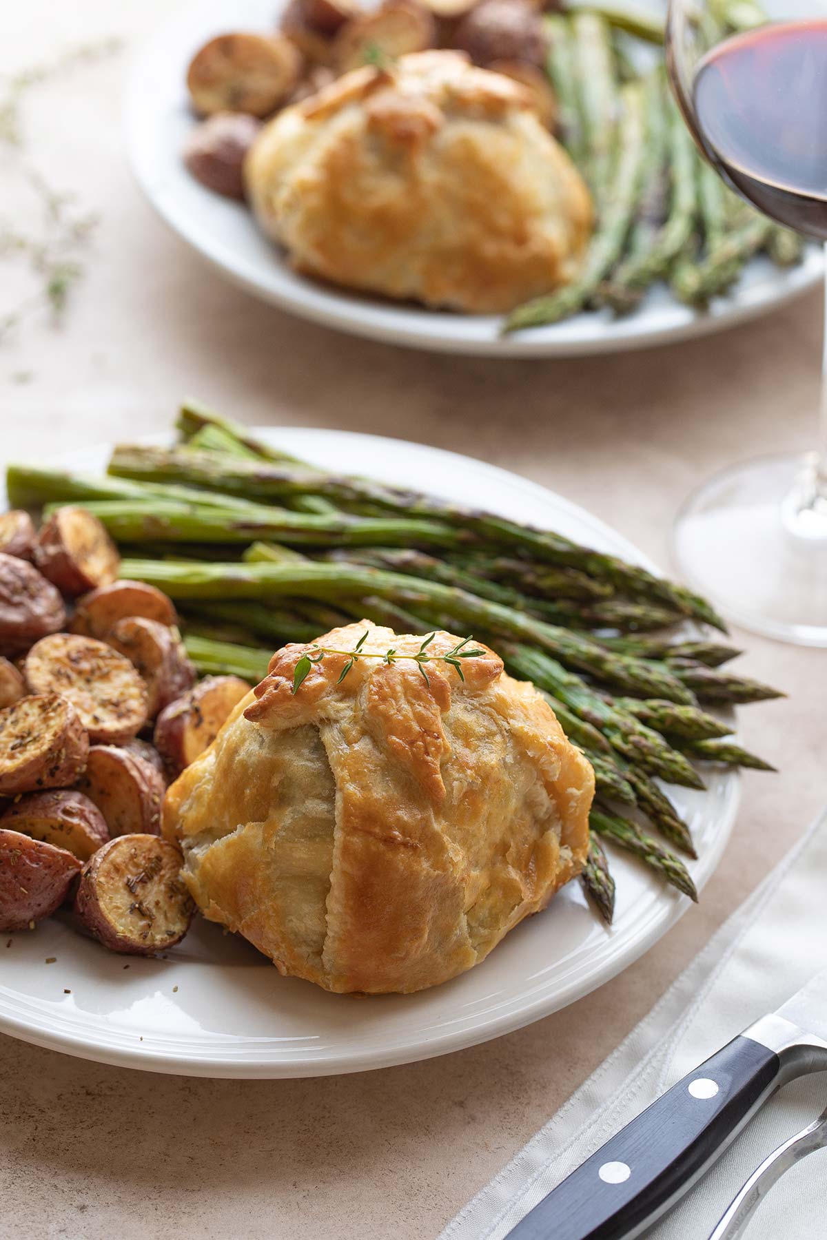 Beef Wellington dinner for two - each uncut, served with potatoes and asparagus - with wine glass and silverware.