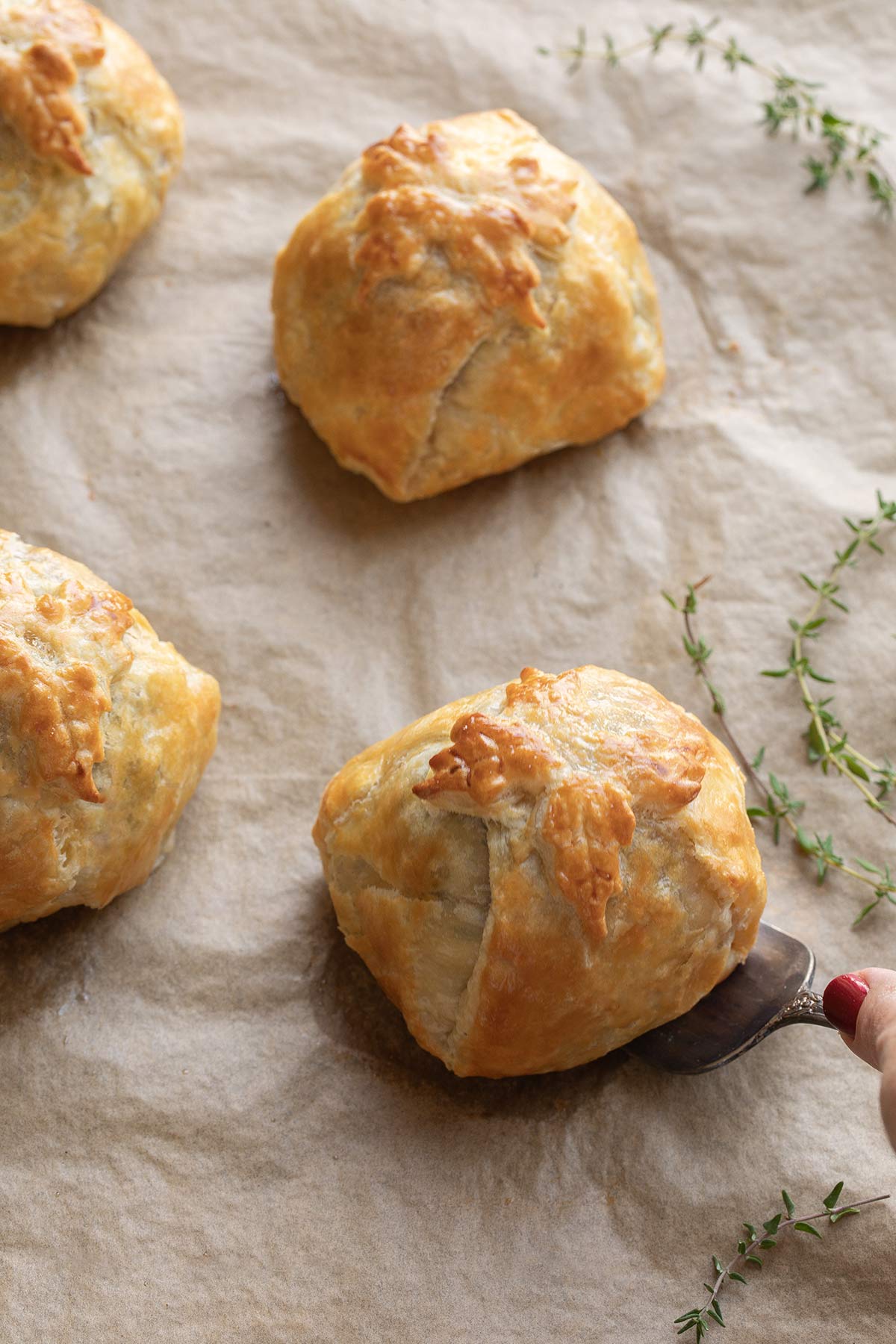 Closeup of baked Wellingtons on parchment, with server scooping under one to serve it.