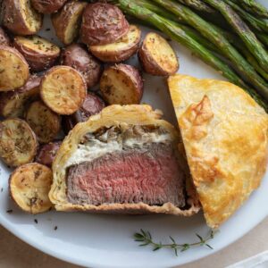 Closeup of one mini Wellington on dinner plate with veggies, cut in half with one half laying up so you can see inside.