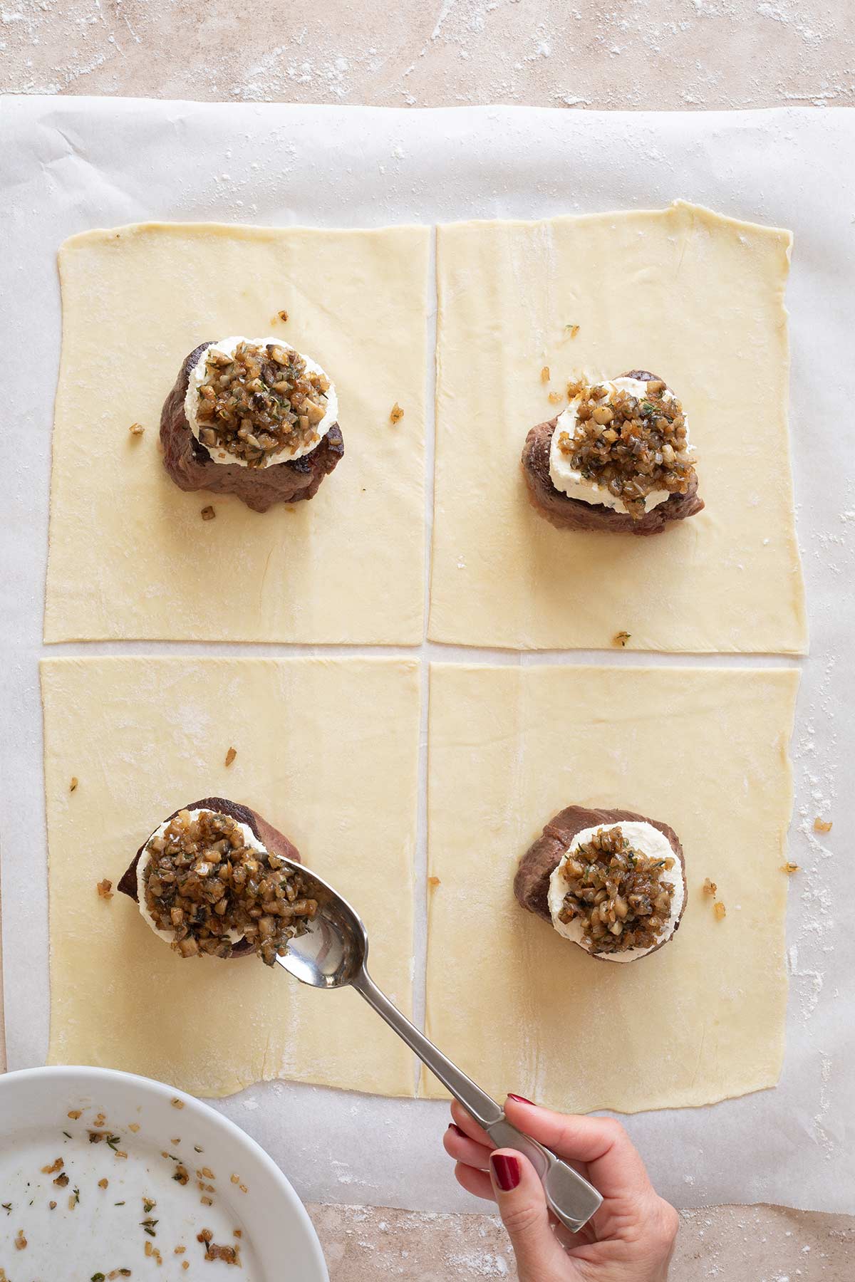 Hand spooning mushroom duxelles on top of the cheese layer on each filet mignon.