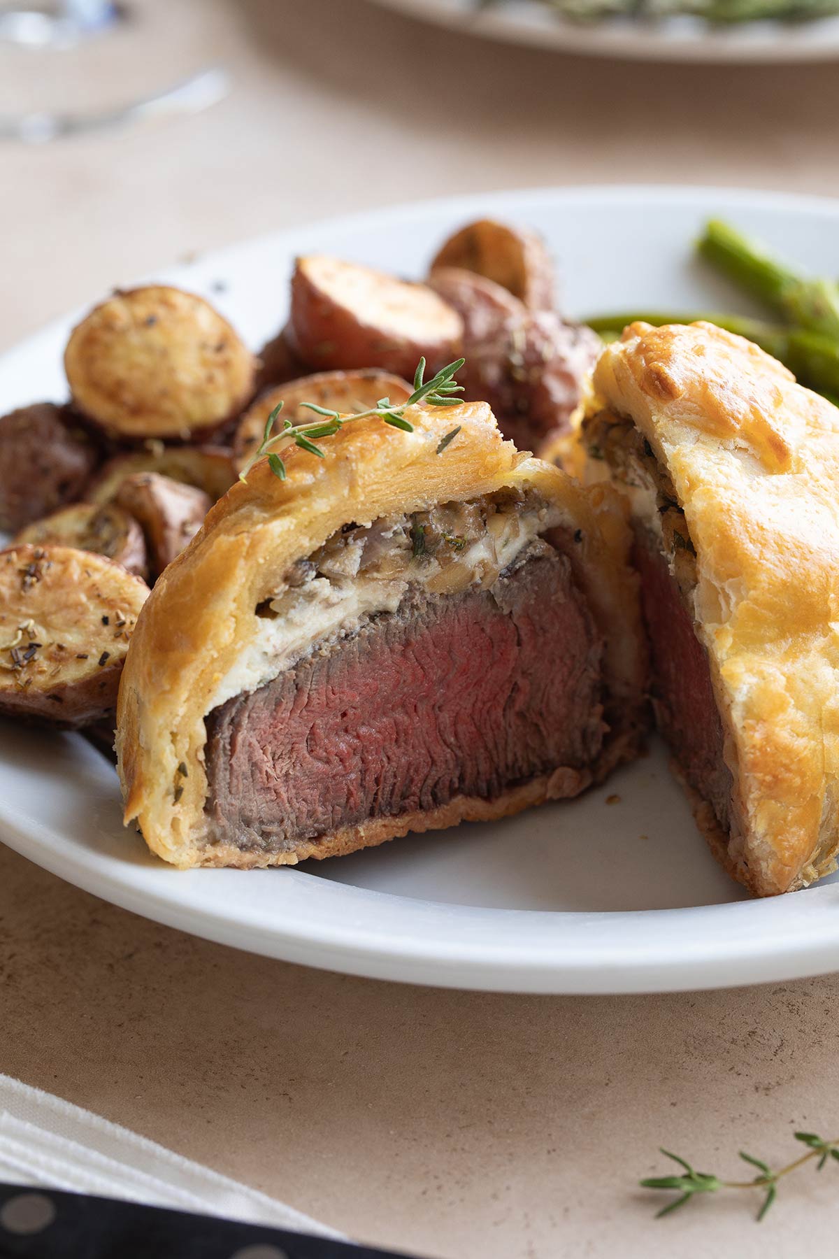 Individual Wellington cut open on white dinner plate so you can see interior, with red potatoes and asparagus behind.