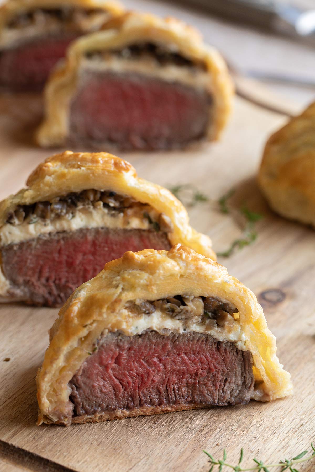 Side view of several individual Wellingtons on wooden board, cut in half to show beef and fillings inside.