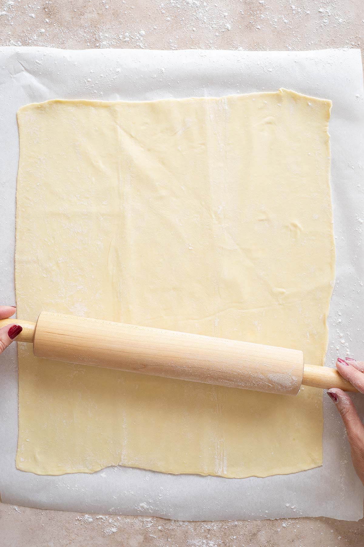 Hands using rolling pin to roll out puff pastry.